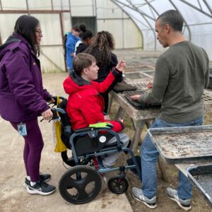 People working in a greenhouse. One person in a red jacket is in a wheel chair