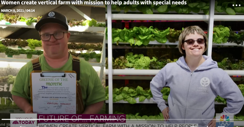 two people stand proudly in front of the green they are growing under lights vertically.