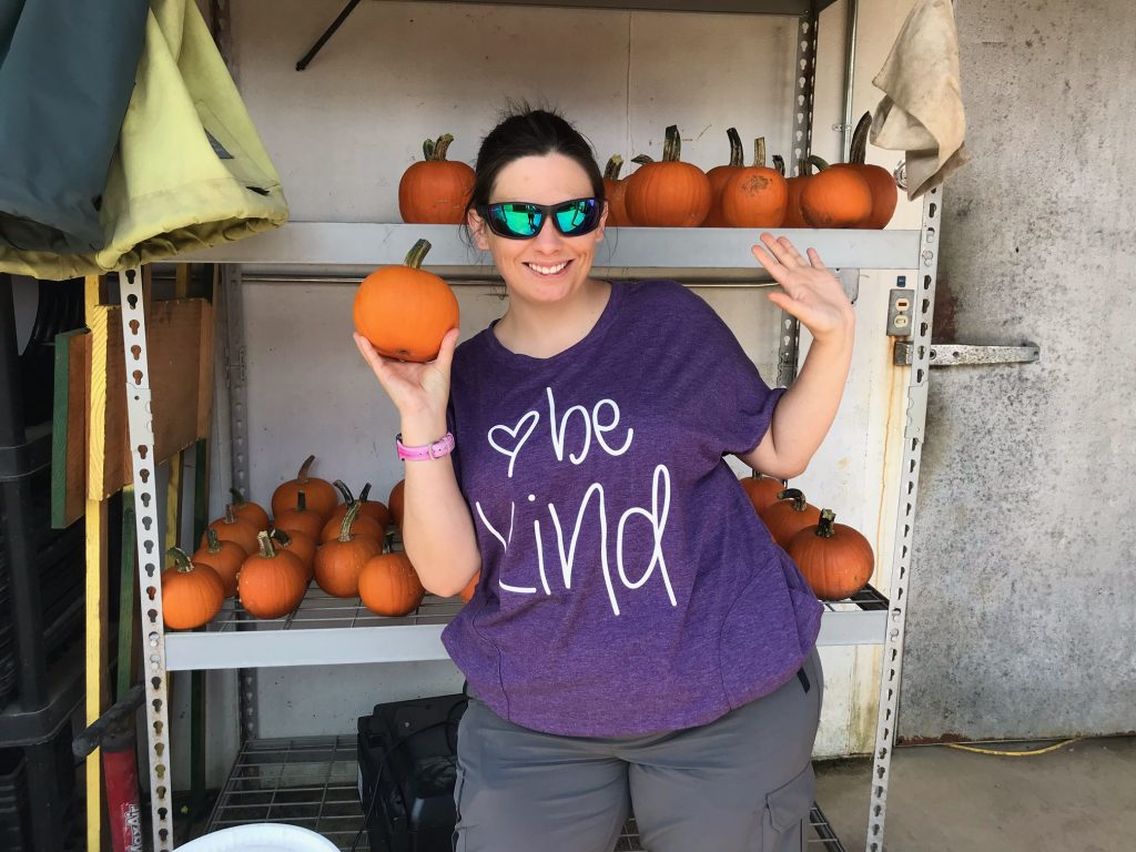 Woman wearing "Be Kind" shirt holding pumpkin